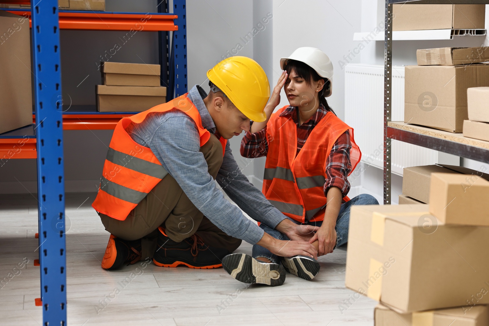 Photo of Accident at work. Man helping his injured colleague in warehouse