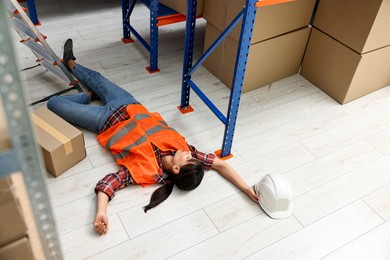 Photo of Accident at work. Unconscious woman lying on floor in warehouse