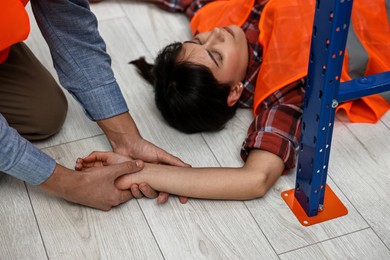 Photo of Accident at work. Man checking pulse of his unconscious colleague in warehouse, closeup