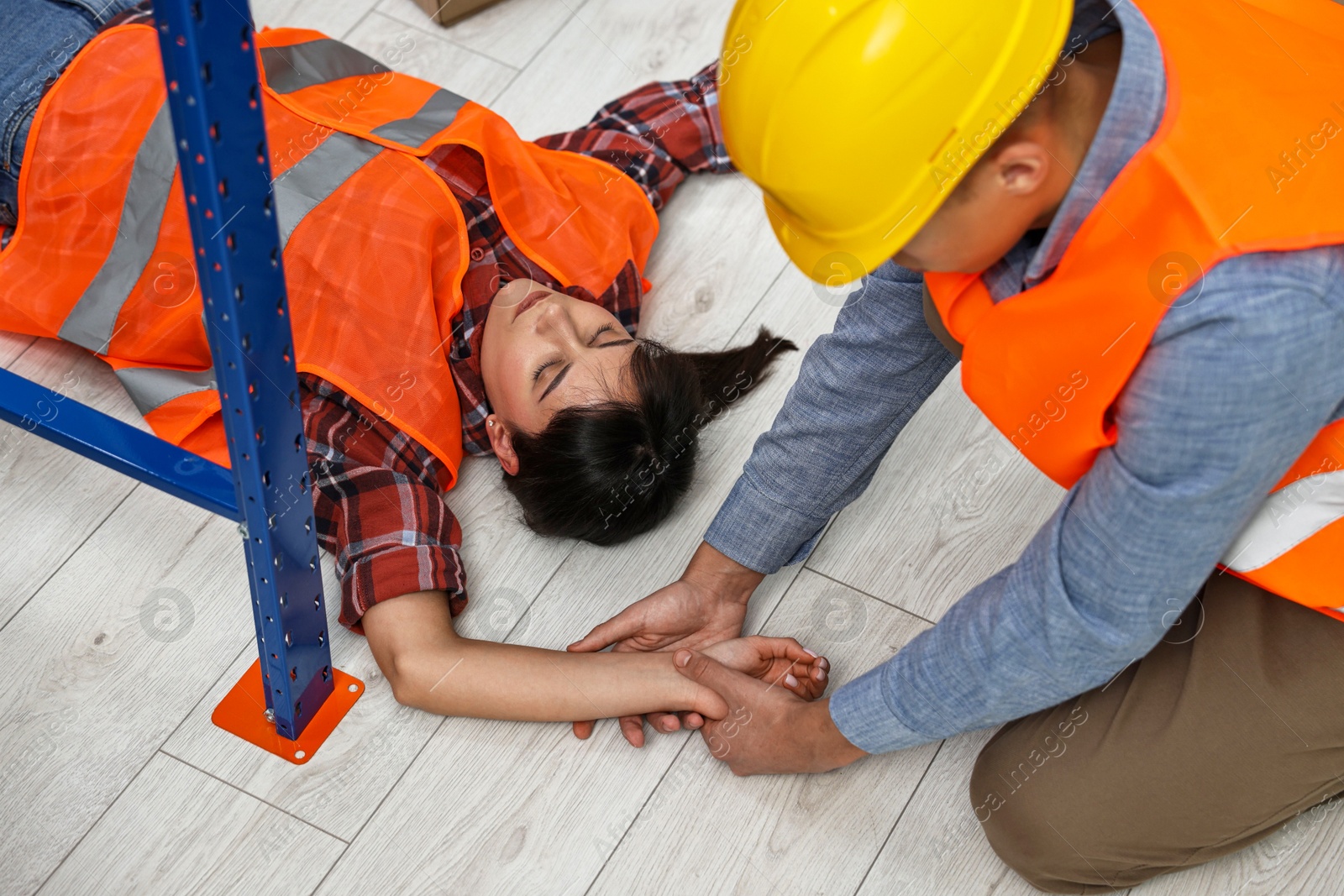 Photo of Accident at work. Man checking pulse of his unconscious colleague in warehouse