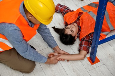 Photo of Accident at work. Man checking pulse of his unconscious colleague in warehouse