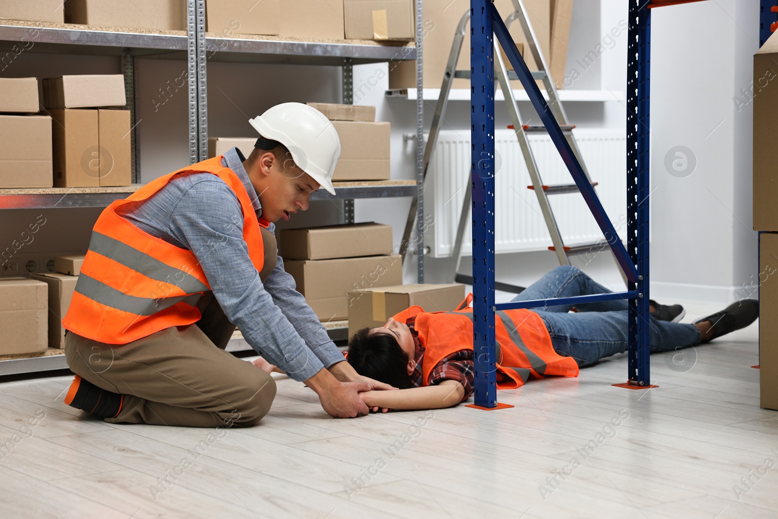 Photo of Accident at work. Man checking pulse of his unconscious colleague in warehouse