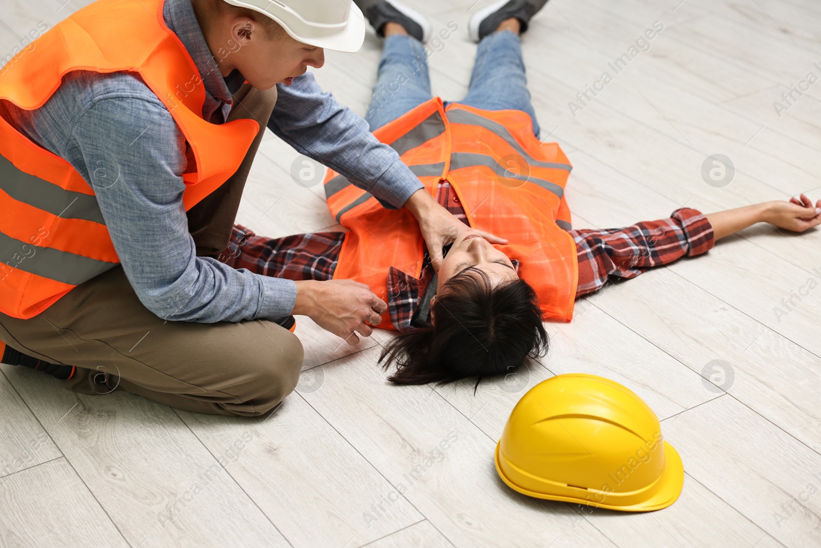 Photo of Accident at work. Man checking pulse of his unconscious colleague in warehouse