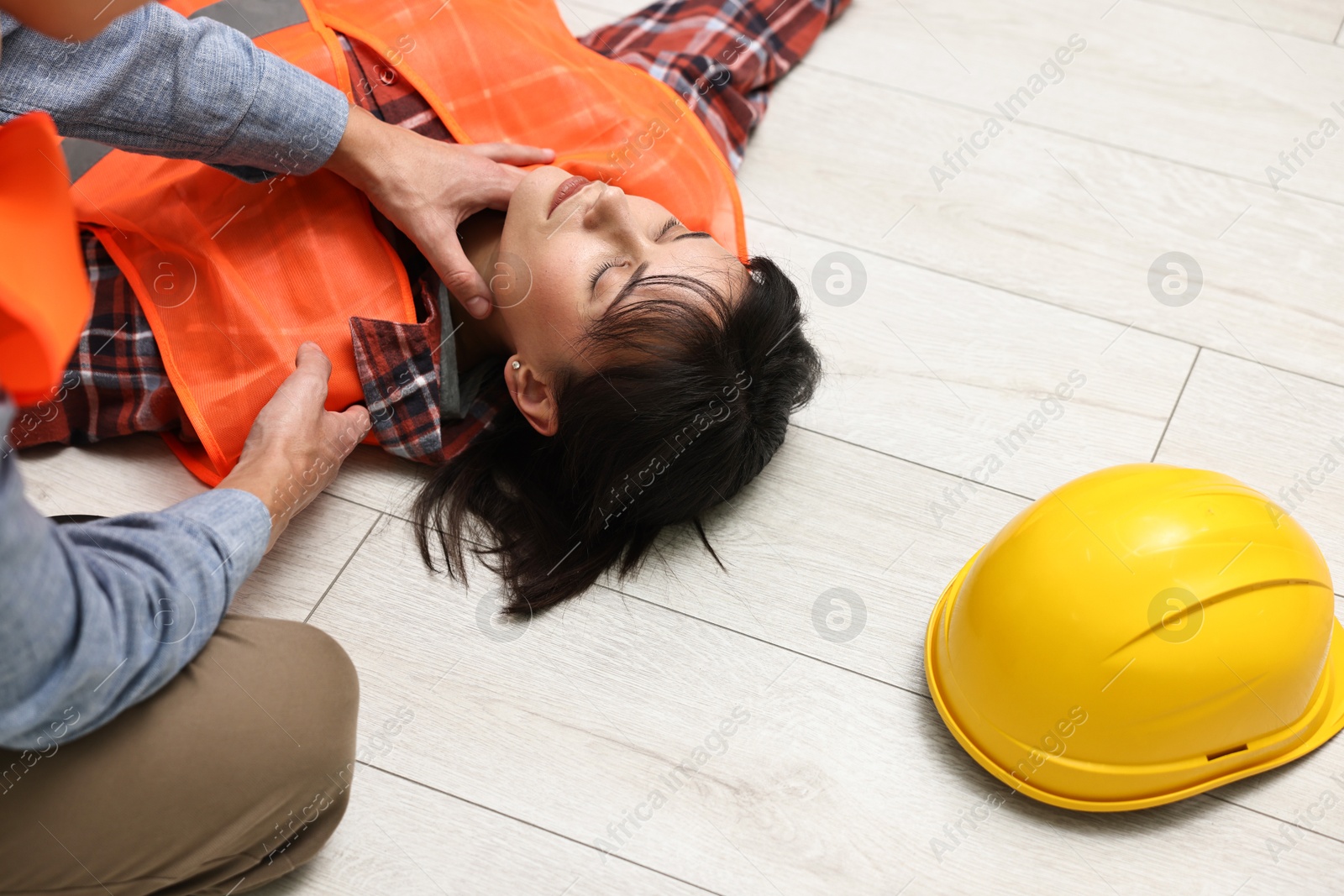 Photo of Accident at work. Man checking pulse of his unconscious colleague in warehouse, closeup