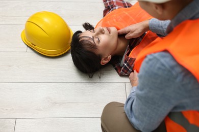 Photo of Accident at work. Man checking pulse of his unconscious colleague in warehouse, closeup