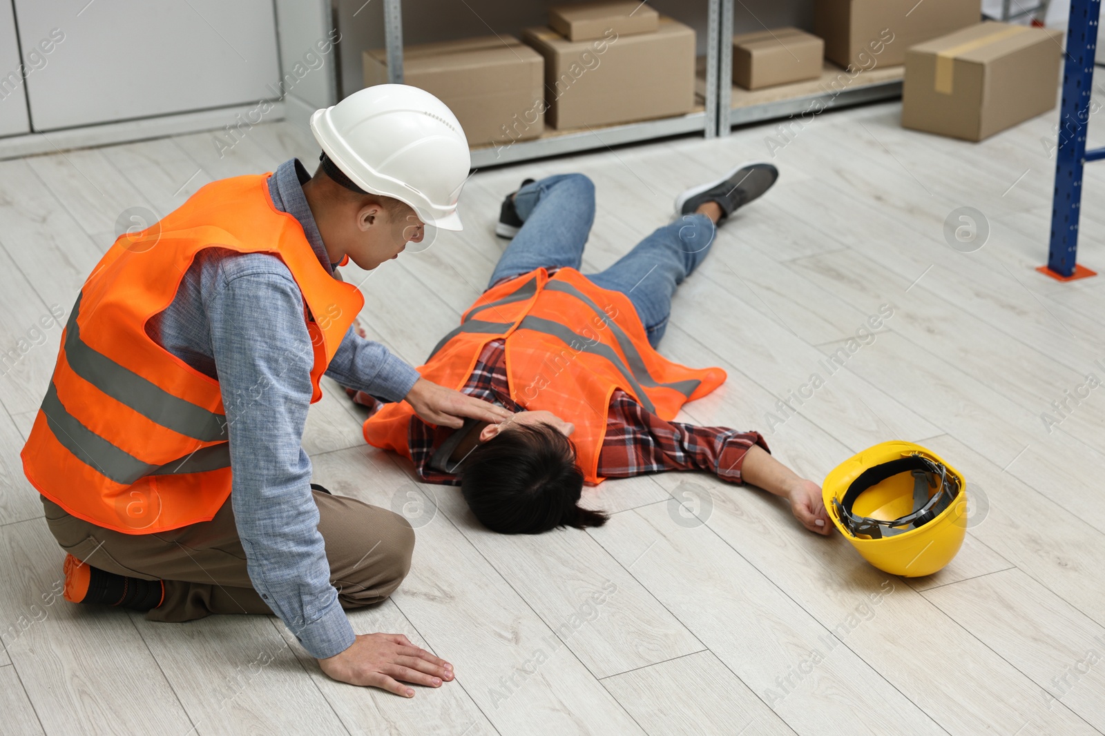 Photo of Accident at work. Man checking pulse of his unconscious colleague in warehouse