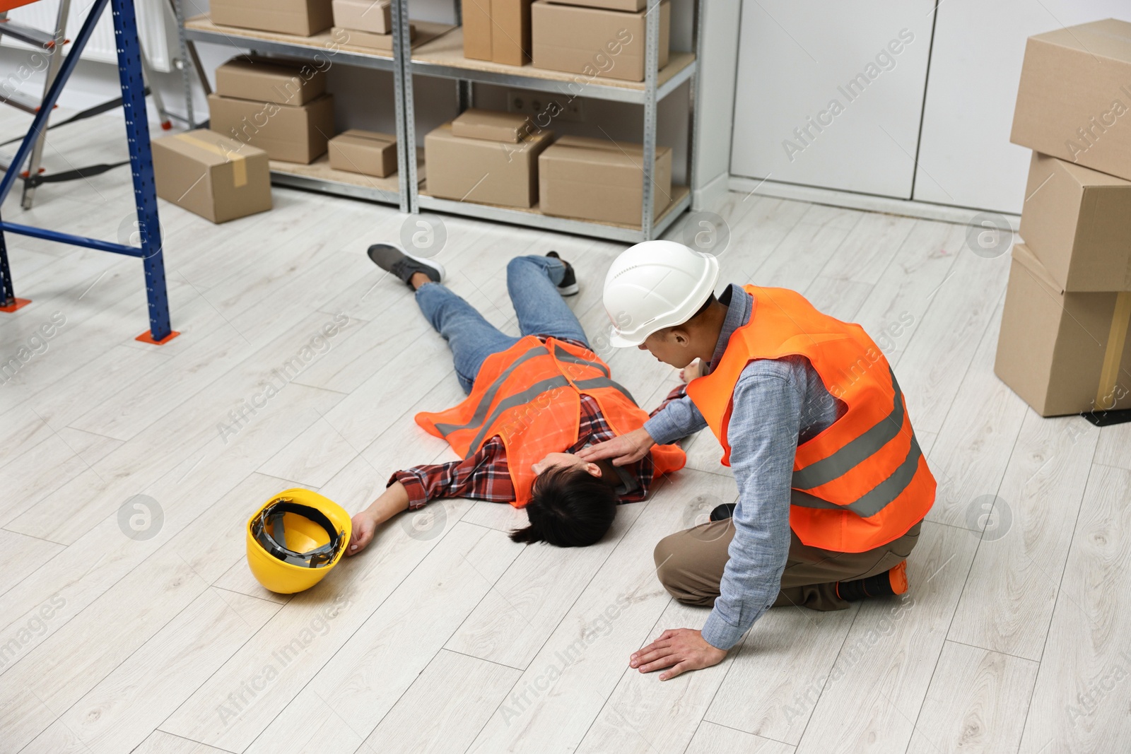 Photo of Accident at work. Man checking pulse of his unconscious colleague in warehouse