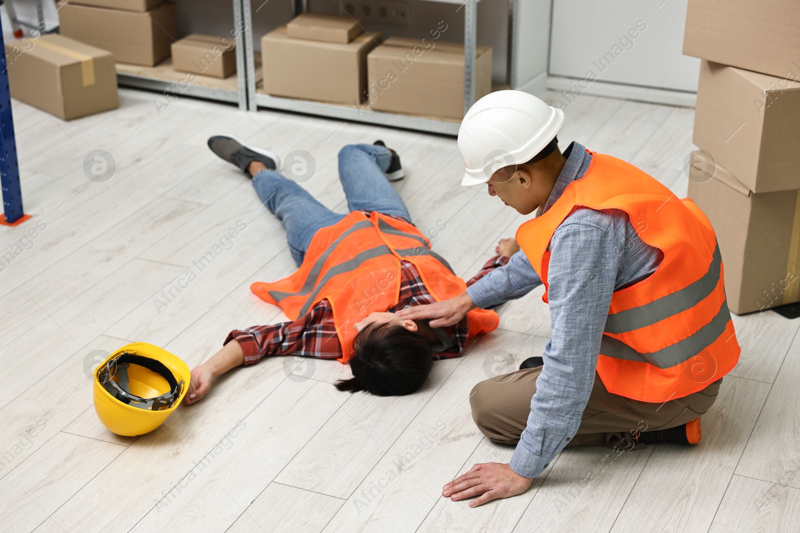 Photo of Accident at work. Man checking pulse of his unconscious colleague in warehouse