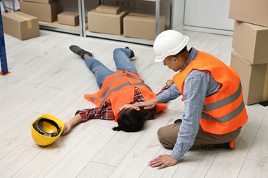 Photo of Accident at work. Man checking pulse of his unconscious colleague in warehouse