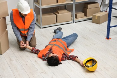 Photo of Accident at work. Man checking pulse of his unconscious colleague in warehouse