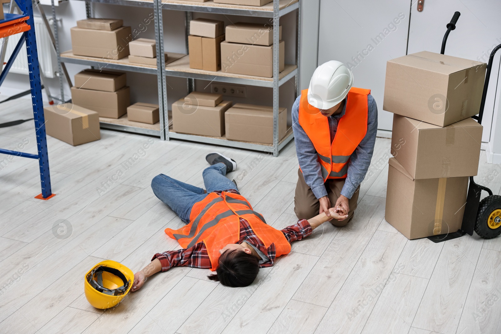 Photo of Accident at work. Man checking pulse of his unconscious colleague in warehouse