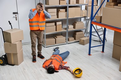 Photo of Accident at work. Worried man and his unconscious colleague in warehouse