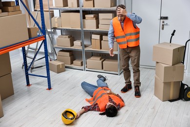 Photo of Accident at work. Worried man and his unconscious colleague in warehouse