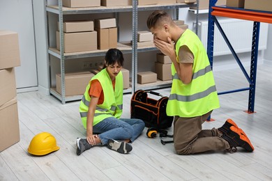 Photo of Accident at work. Worried man and his injured colleague in warehouse