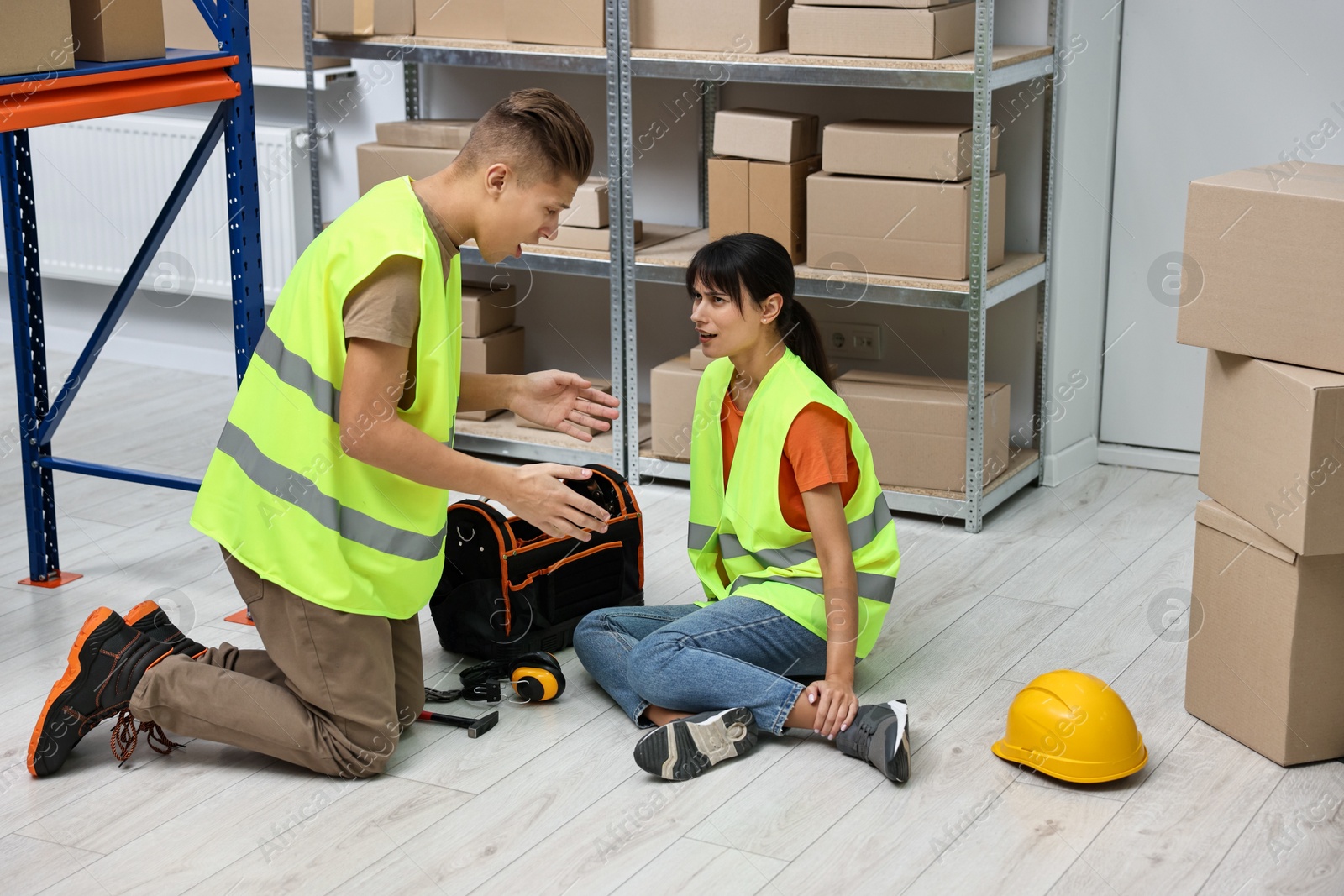 Photo of Accident at work. Man helping his injured colleague in warehouse