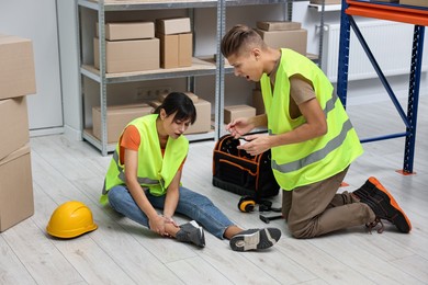 Photo of Accident at work. Man helping his injured colleague in warehouse