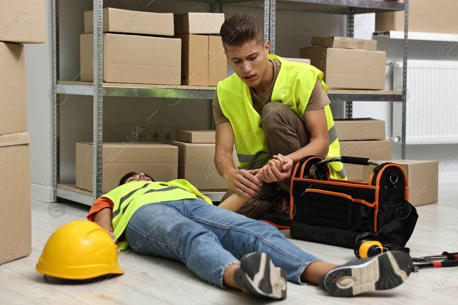 Photo of Accident at work. Man checking pulse of his unconscious colleague in warehouse