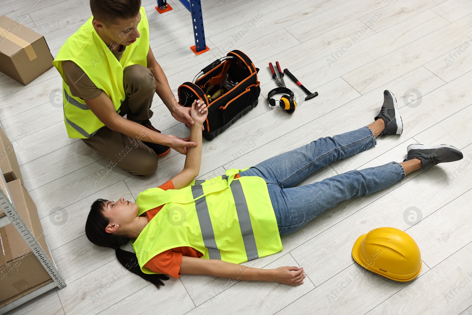 Photo of Accident at work. Man checking pulse of his unconscious colleague in warehouse