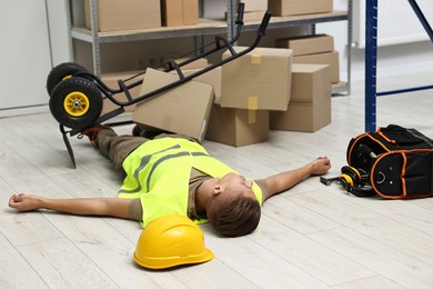 Photo of Accident at work. Unconscious man and overturned hand truck on floor in warehouse