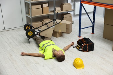 Photo of Accident at work. Unconscious man and overturned hand truck on floor in warehouse