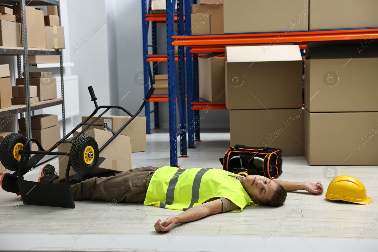 Photo of Accident at work. Unconscious man and overturned hand truck on floor in warehouse