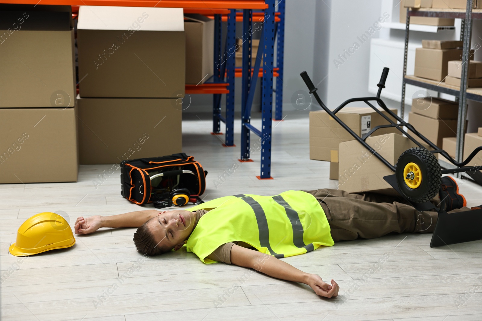 Photo of Accident at work. Unconscious man and overturned hand truck on floor in warehouse