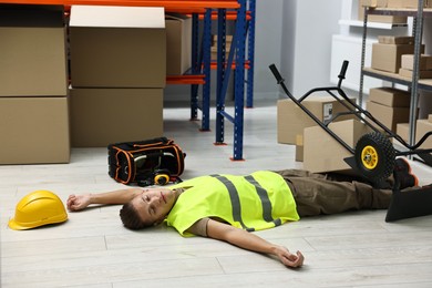 Photo of Accident at work. Unconscious man and overturned hand truck on floor in warehouse