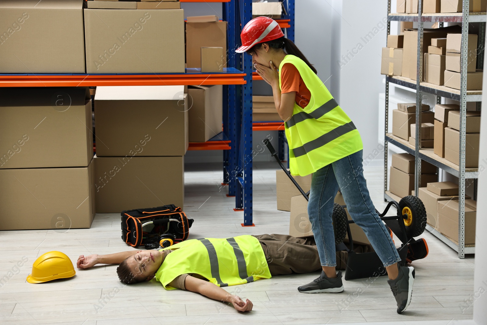 Photo of Accident at work. Worried woman and her unconscious colleague in warehouse