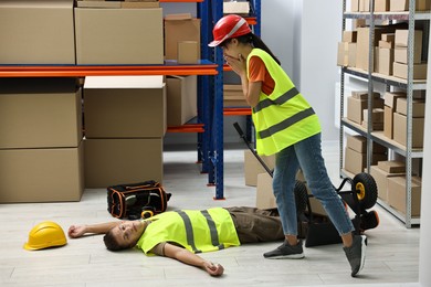 Photo of Accident at work. Worried woman and her unconscious colleague in warehouse