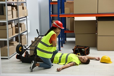 Photo of Accident at work. Worried woman and her unconscious colleague in warehouse