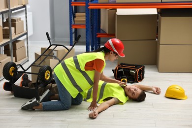 Photo of Accident at work. Woman checking pulse of her unconscious colleague in warehouse