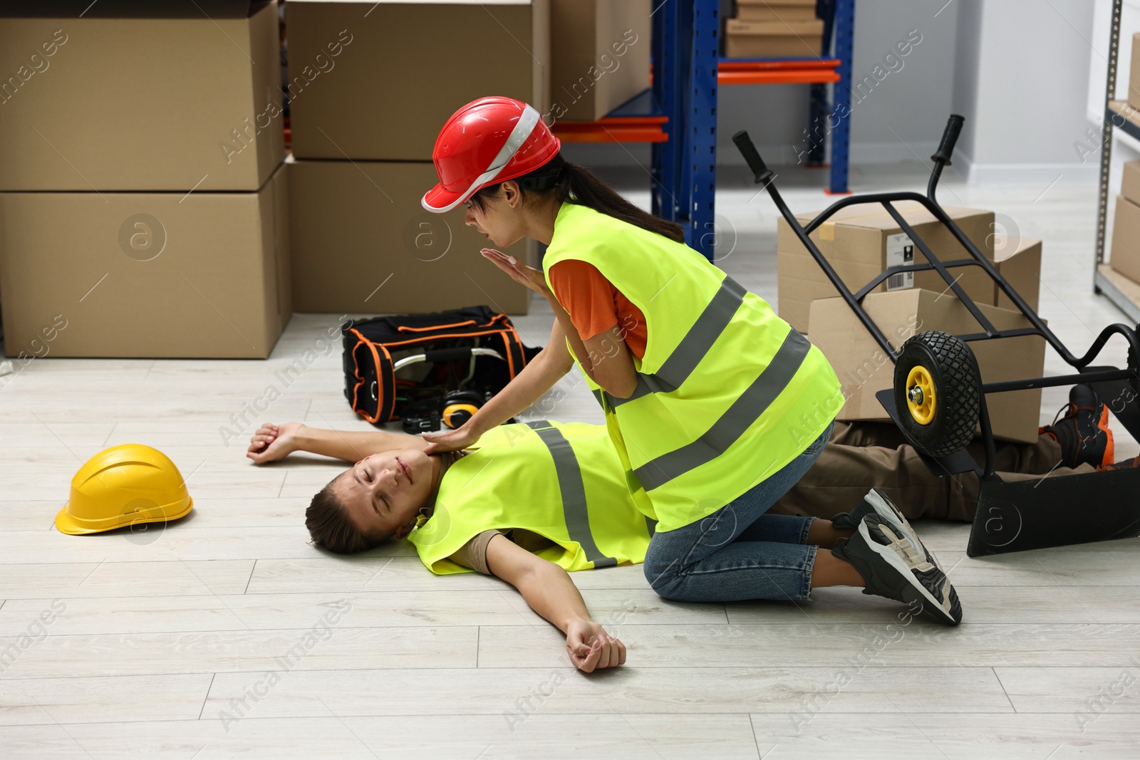 Photo of Accident at work. Woman checking pulse of her unconscious colleague in warehouse