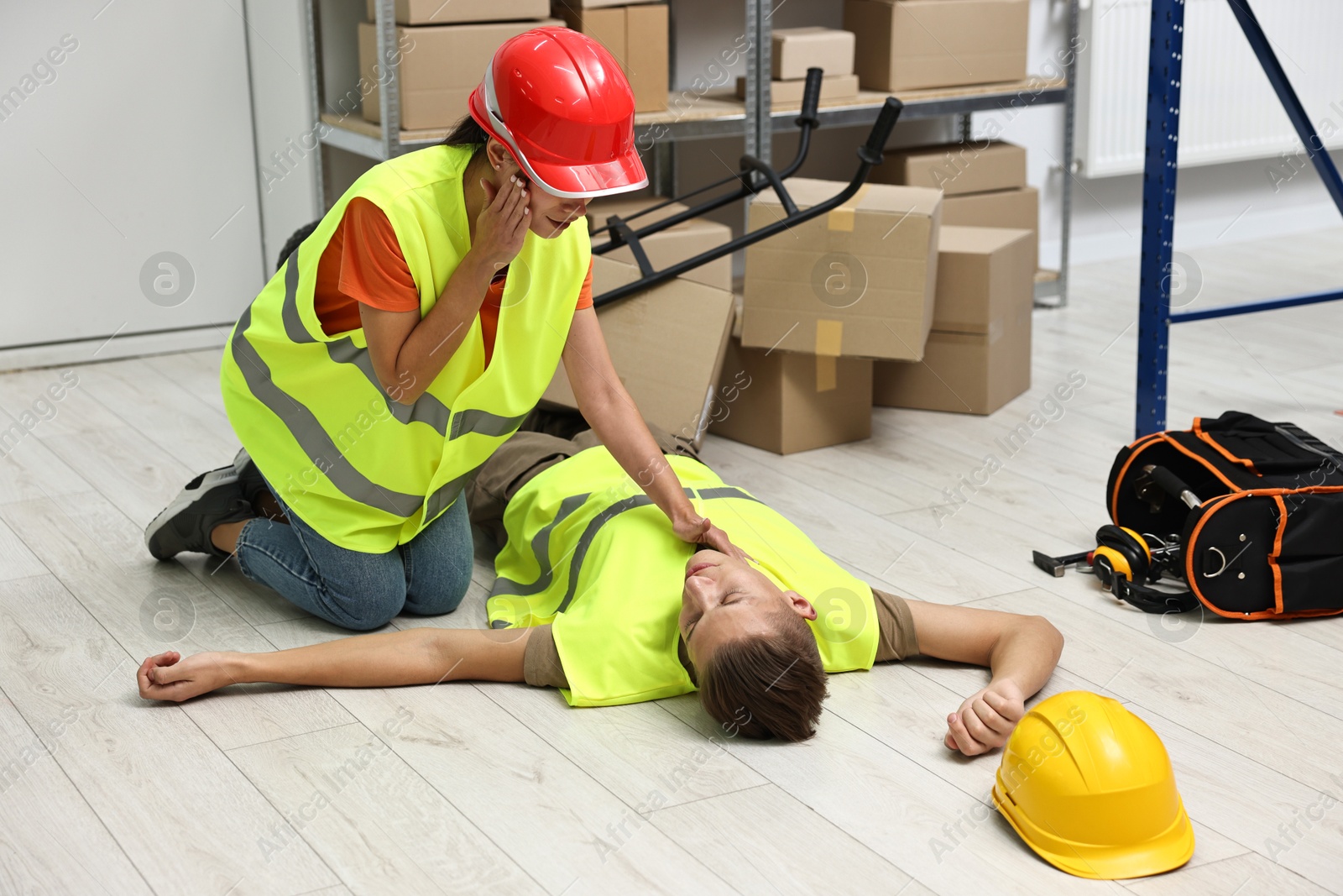 Photo of Accident at work. Woman checking pulse of her unconscious colleague in warehouse