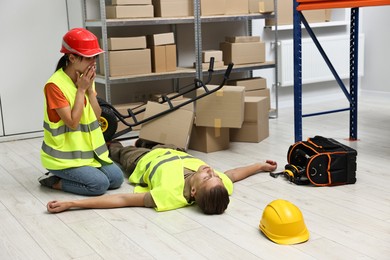 Photo of Accident at work. Worried woman and her unconscious colleague in warehouse