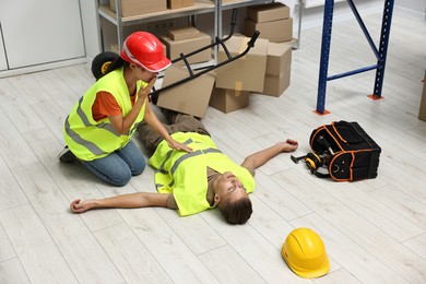 Photo of Accident at work. Worried woman and her unconscious colleague in warehouse