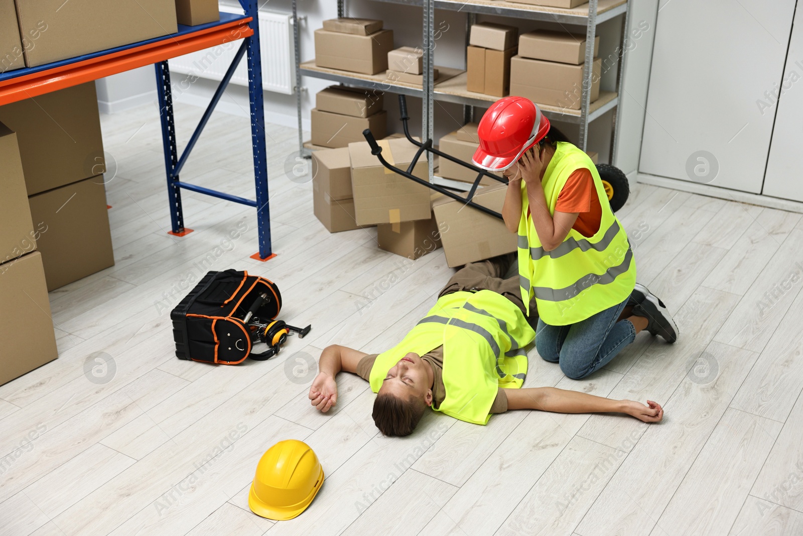 Photo of Accident at work. Worried woman and her unconscious colleague in warehouse