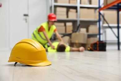 Photo of Accident at work. Hardhat on floor and woman helping her injured colleague in warehouse, selective focus