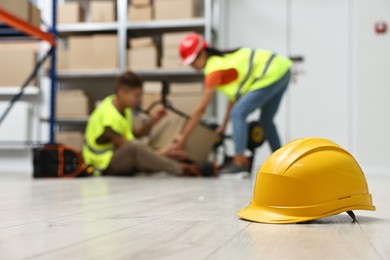 Photo of Accident at work. Hardhat on floor and woman helping her injured colleague in warehouse, selective focus