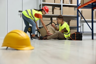 Photo of Accident at work. Hardhat on floor and woman helping her injured colleague in warehouse, selective focus