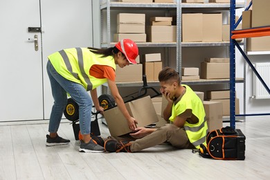 Photo of Accident at work. Woman helping her injured colleague in warehouse