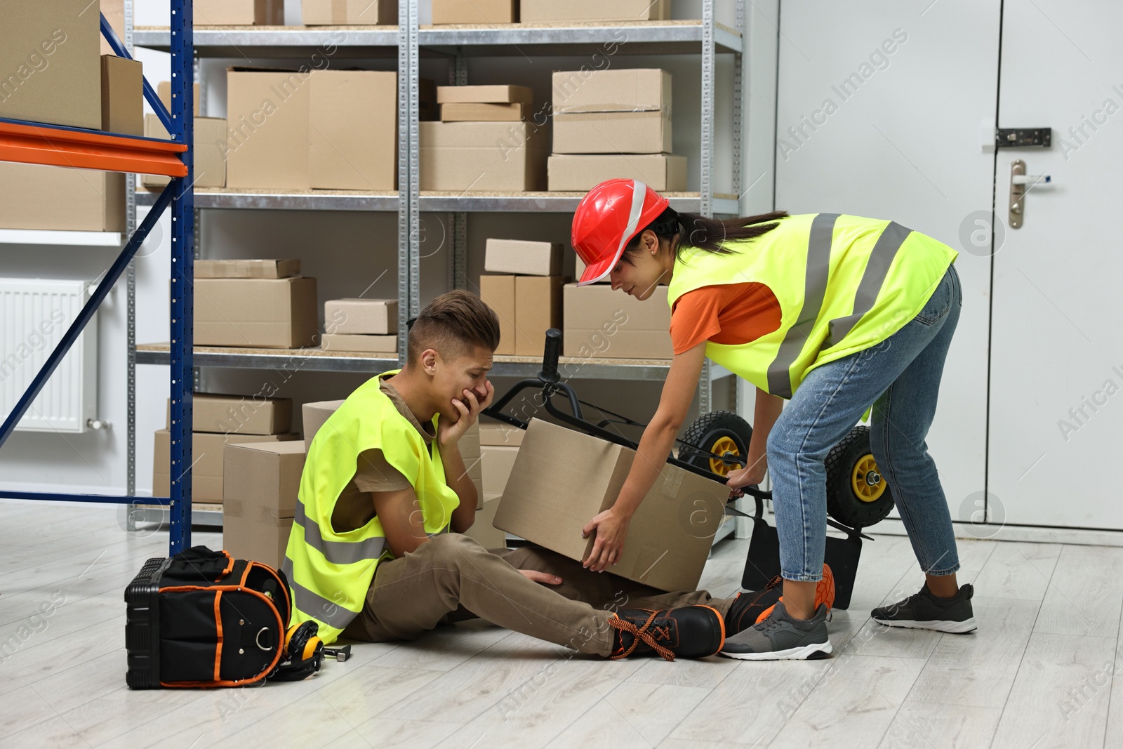 Photo of Accident at work. Woman helping her injured colleague in warehouse