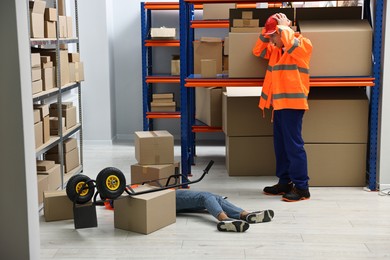 Photo of Accident at work. Worried man and his unconscious colleague in warehouse