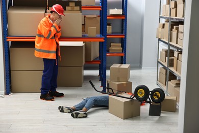 Photo of Accident at work. Worried man and his unconscious colleague in warehouse