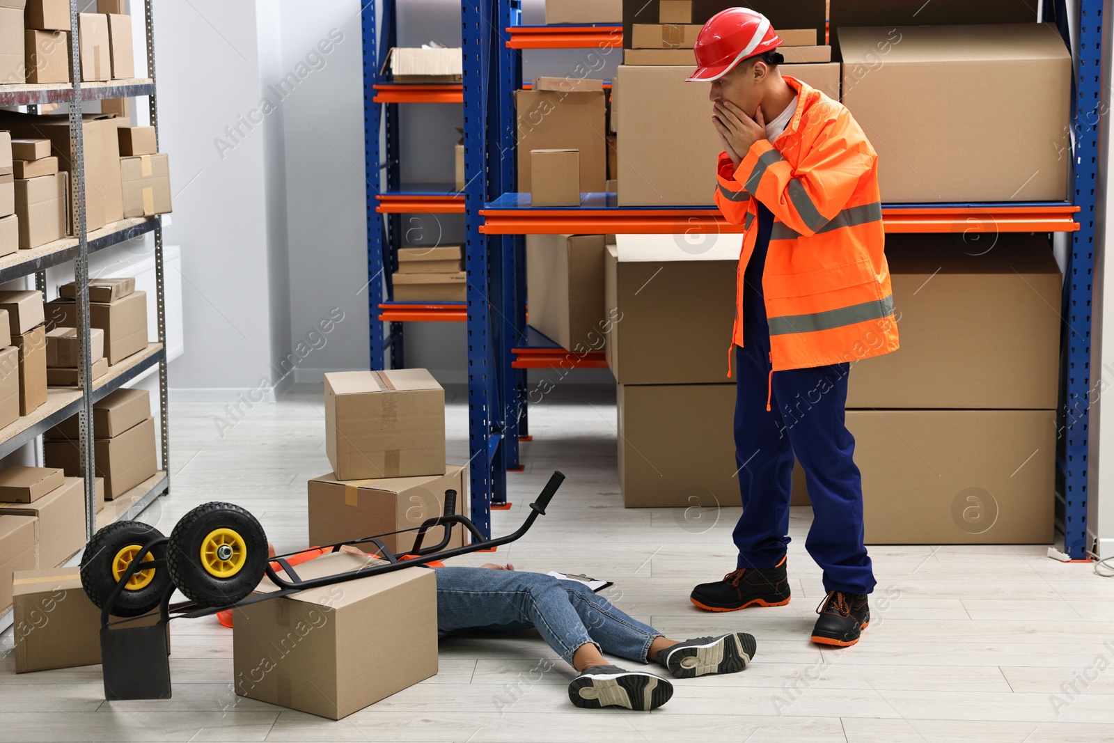 Photo of Accident at work. Worried man and his unconscious colleague in warehouse