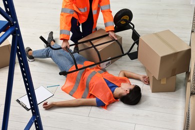 Photo of Accident at work. Man helping his unconscious colleague in warehouse