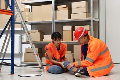 Photo of Accident at work. Man helping his injured colleague in warehouse