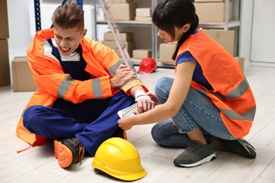 Accident at work. Woman putting bandage on her colleague's injured wrist in warehouse