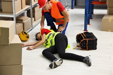 Accident at work. Man helping his unconscious colleague in warehouse