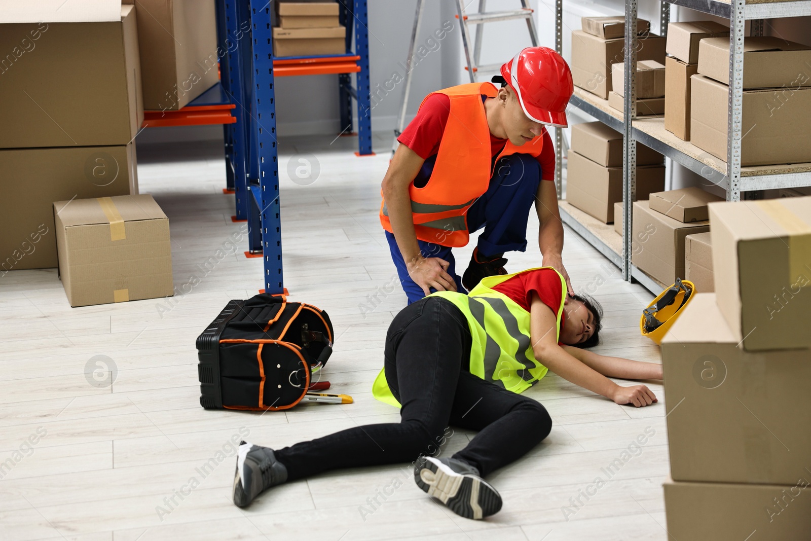 Photo of Accident at work. Man helping his unconscious colleague in warehouse