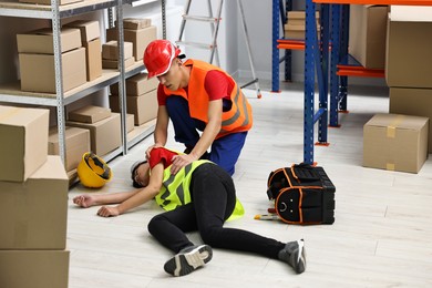 Photo of Accident at work. Man helping his unconscious colleague in warehouse